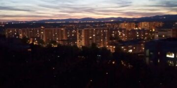 Vista nocturna de edificios de la ciudad y montañas distantes.