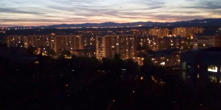 Vista nocturna de edificios de la ciudad y montañas distantes.