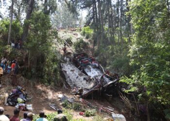 Los trabajadores de rescate buscan en los restos de un accidente de autobús en un área boscosa mientras los espectadores observan.