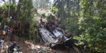 Los trabajadores de rescate buscan en los restos de un accidente de autobús en un área boscosa mientras los espectadores observan.