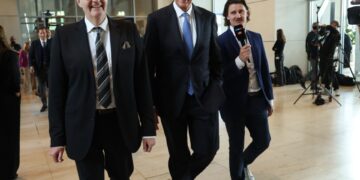 Friedrich Merz, canciller alemán designado, con otros dos hombres, uno de los cuales sostiene un micrófono.