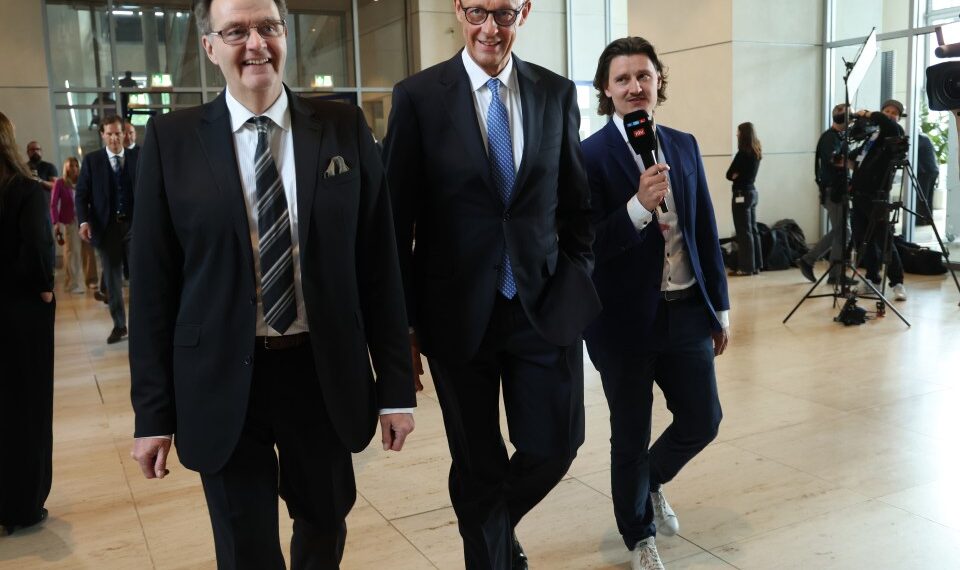 Friedrich Merz, canciller alemán designado, con otros dos hombres, uno de los cuales sostiene un micrófono.