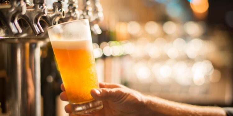 Una mano que sostiene un vaso de cerveza de cerveza que se vierte de un grifo.