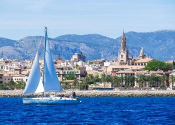 Sailboat en Palma de Mallorca Harbour con ciudad y montañas en el fondo.