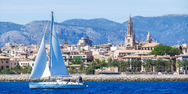 Sailboat en Palma de Mallorca Harbour con ciudad y montañas en el fondo.