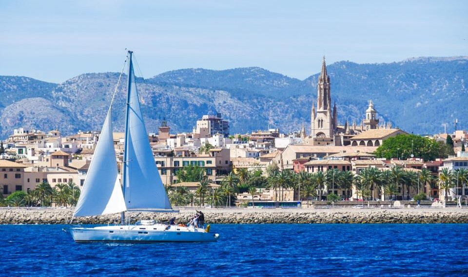 Sailboat en Palma de Mallorca Harbour con ciudad y montañas en el fondo.