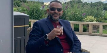 Hombre sentado al aire libre en una mesa, disfrutando de una bebida.