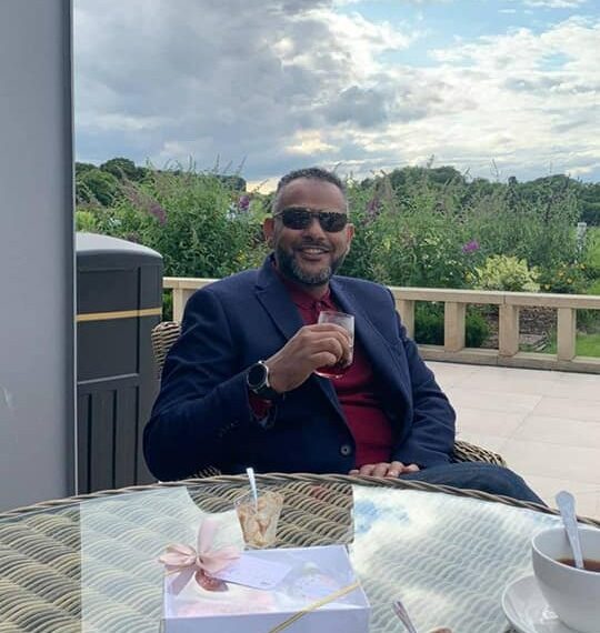 Hombre sentado al aire libre en una mesa, disfrutando de una bebida.
