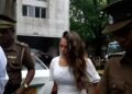 Una mujer joven con un vestido blanco escoltada por agentes de policía.