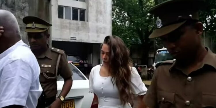 Una mujer joven con un vestido blanco escoltada por agentes de policía.