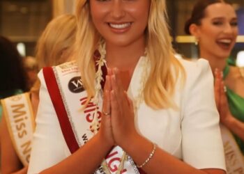 Miss Inglaterra, Milla Magee, con un vestido blanco y faja, realizando un saludo tradicional.