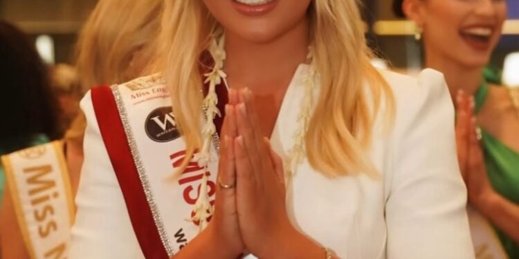 Miss Inglaterra, Milla Magee, con un vestido blanco y faja, realizando un saludo tradicional.