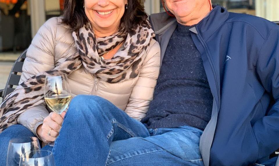 Alan y Karen Carter sentados juntos al aire libre con vino.