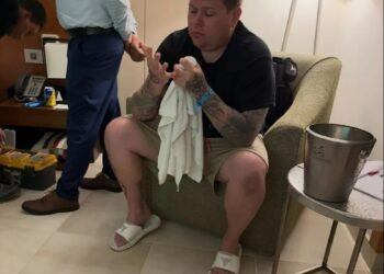 Hombre sentado en una habitación de hotel, sosteniendo una toalla y mirando sus manos.