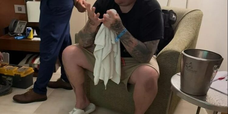 Hombre sentado en una habitación de hotel, sosteniendo una toalla y mirando sus manos.