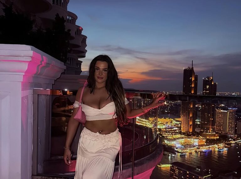 Mujer con atuendo blanco en la azotea con vistas a la ciudad al atardecer.