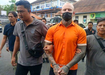 Un boxeador británico esposado, con un mono naranja, es escoltado por la policía.