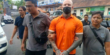 Un boxeador británico esposado, con un mono naranja, es escoltado por la policía.