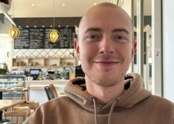 Retrato de un joven con una cabeza afeitada, sonriendo, con una sudadera con capucha.