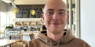 Retrato de un joven con una cabeza afeitada, sonriendo, con una sudadera con capucha.