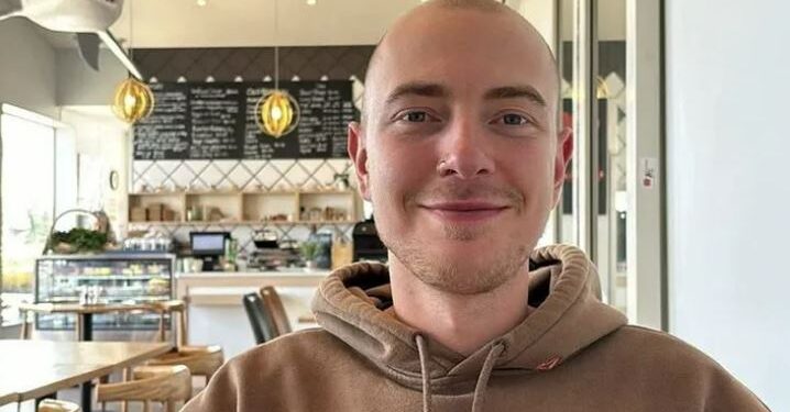Retrato de un joven con una cabeza afeitada, sonriendo, con una sudadera con capucha.