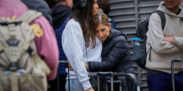 Dos mujeres se abrazan en una estación de tren mientras esperan noticias sobre trenes retrasados.