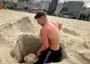 Hombre cavando un agujero en la arena en una playa.