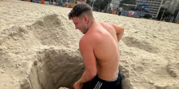 Hombre cavando un agujero en la arena en una playa.