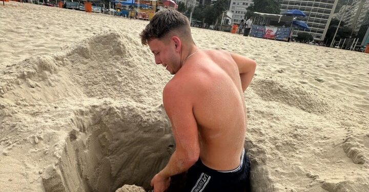 Hombre cavando un agujero en la arena en una playa.