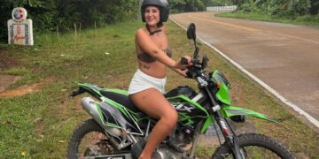 Mujer joven sentada en una motocicleta verde en Tailandia.