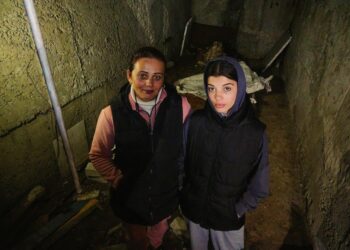 Dos mujeres paradas en un sótano oscuro y dañado.