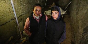 Dos mujeres paradas en un sótano oscuro y dañado.