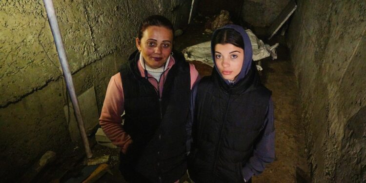 Dos mujeres paradas en un sótano oscuro y dañado.