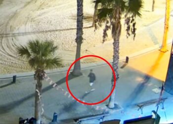 Imagen de CCTV de una persona que camina en un área pavimentada cerca de una playa por la noche.