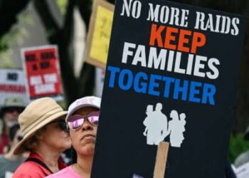 Una persona tiene una señal que lee "No más incursiones; Mantenga a las familias juntas" Durante una protesta al aire libre