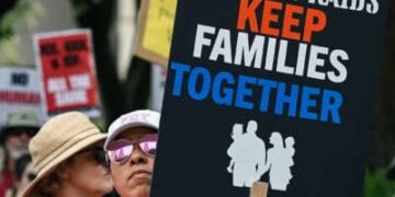 Una persona tiene una señal que lee "No más incursiones; Mantenga a las familias juntas" Durante una protesta al aire libre