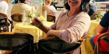 Mujer sentada en un café al aire libre con una copa de vino blanco, Duomo di Milano en el fondo.