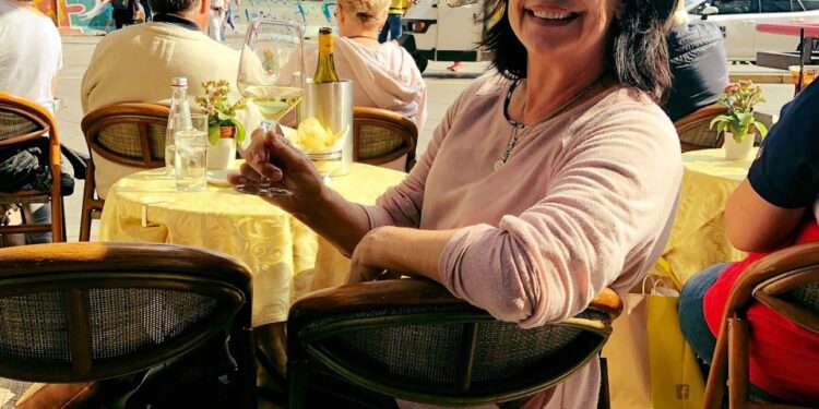 Mujer sentada en un café al aire libre con una copa de vino blanco, Duomo di Milano en el fondo.