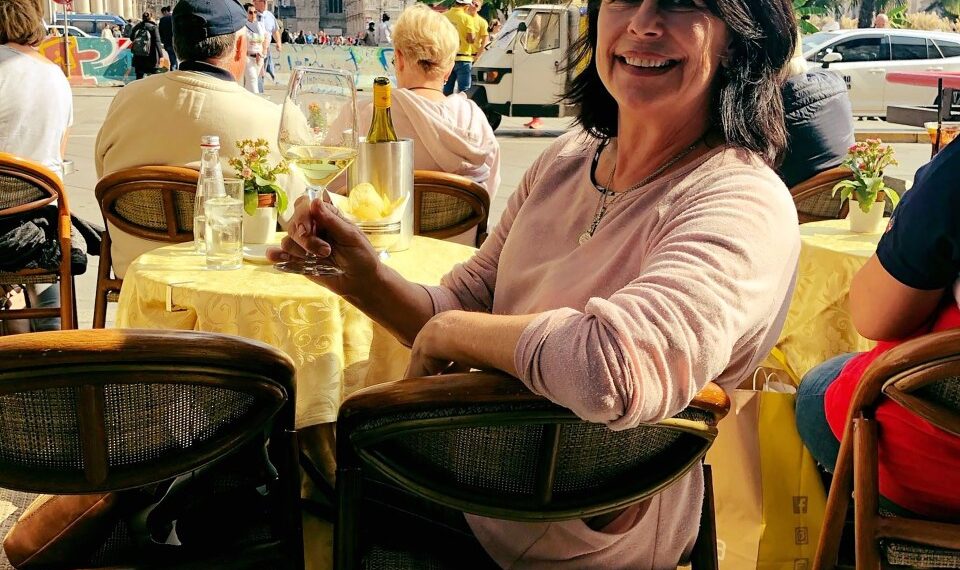 Mujer sentada en un café al aire libre con una copa de vino blanco, Duomo di Milano en el fondo.
