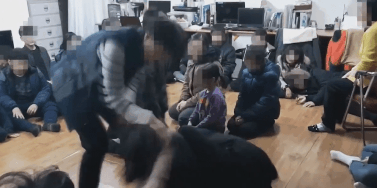 Una persona que interactúa con un grupo de niños sentados en el piso.