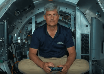 Hombre en camisa de Oceangate sentado en un sumergible, sosteniendo un controlador.