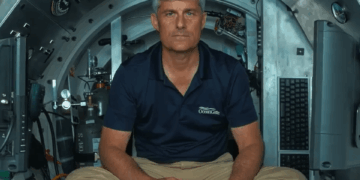 Hombre en camisa de Oceangate sentado en un sumergible, sosteniendo un controlador.