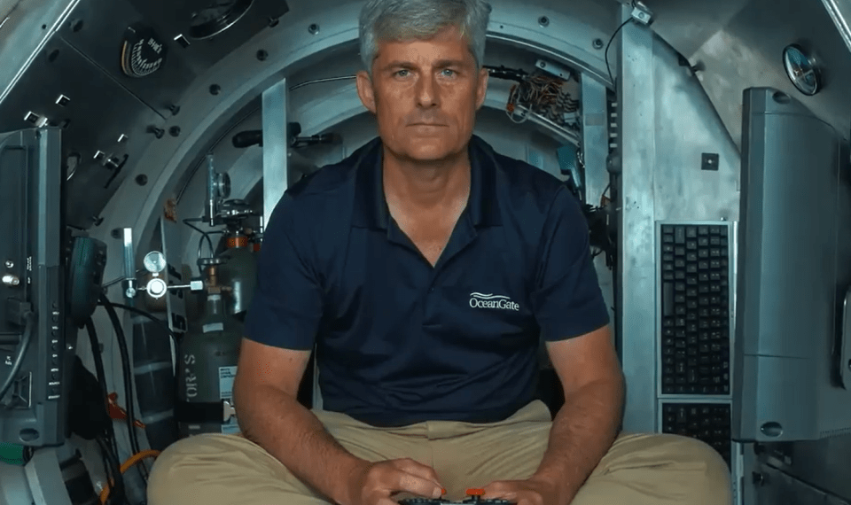 Hombre en camisa de Oceangate sentado en un sumergible, sosteniendo un controlador.