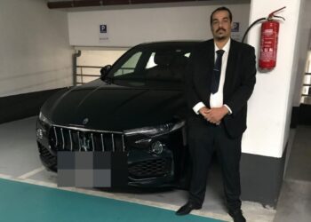 El taxista Nasim Mumin de pie junto a un automóvil negro en un estacionamiento.