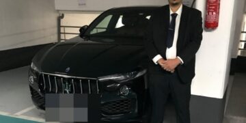 El taxista Nasim Mumin de pie junto a un automóvil negro en un estacionamiento.