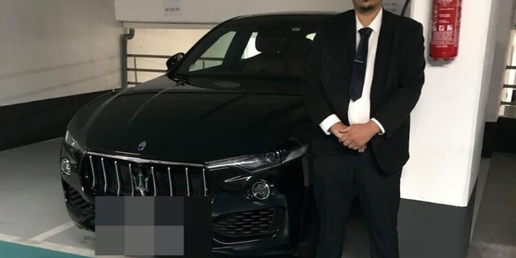 El taxista Nasim Mumin de pie junto a un automóvil negro en un estacionamiento.