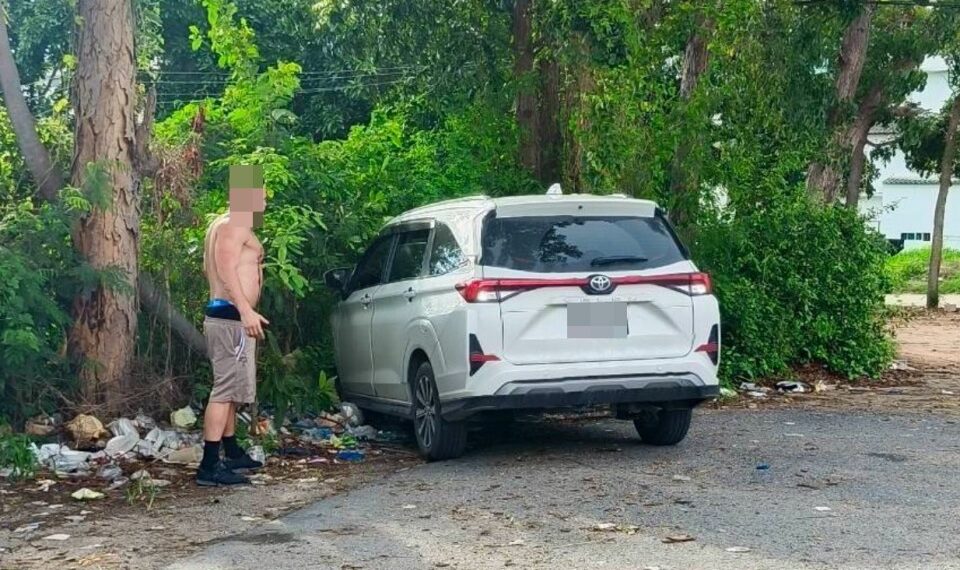 Un hombre sin camisa se encuentra cerca de un Toyota Veloz blanco en un estacionamiento.