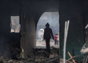 Una niña se encuentra siluada en un arco parcialmente destruido que conduce a una escuela destruida