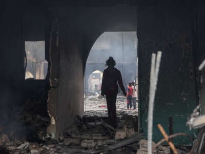 Una niña se encuentra siluada en un arco parcialmente destruido que conduce a una escuela destruida