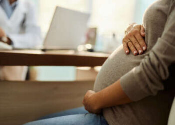 Una persona embarazada consulta con un médico en un escritorio, de cerca en manos del vientre.